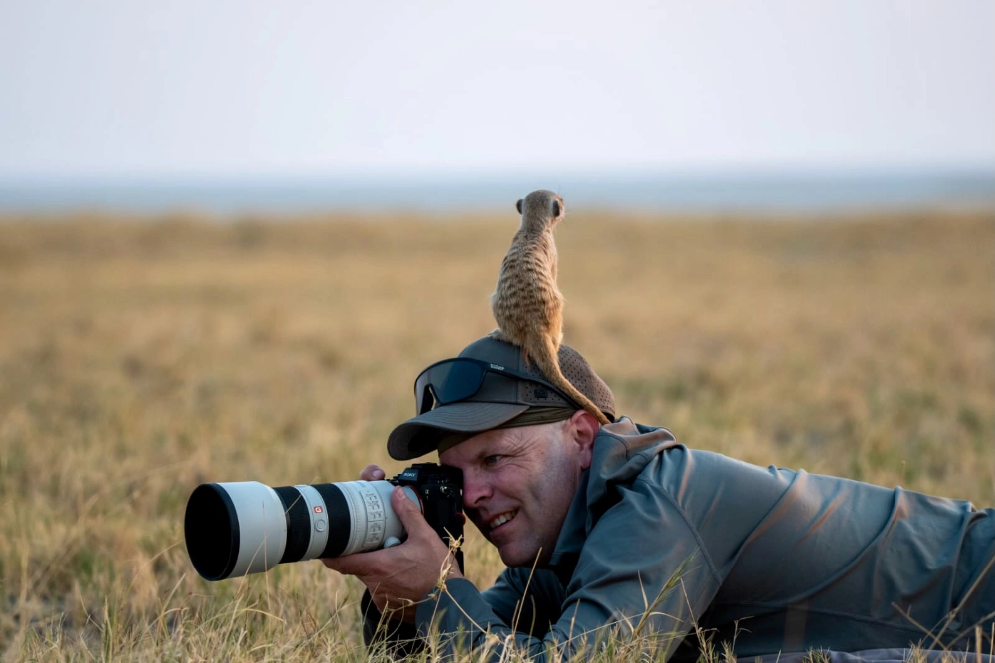 Side view of James taking a picture with a Meerkat sitting on his head.